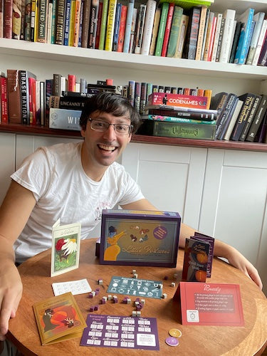 A man who created a baby shower board game displaying the game contents on a table.