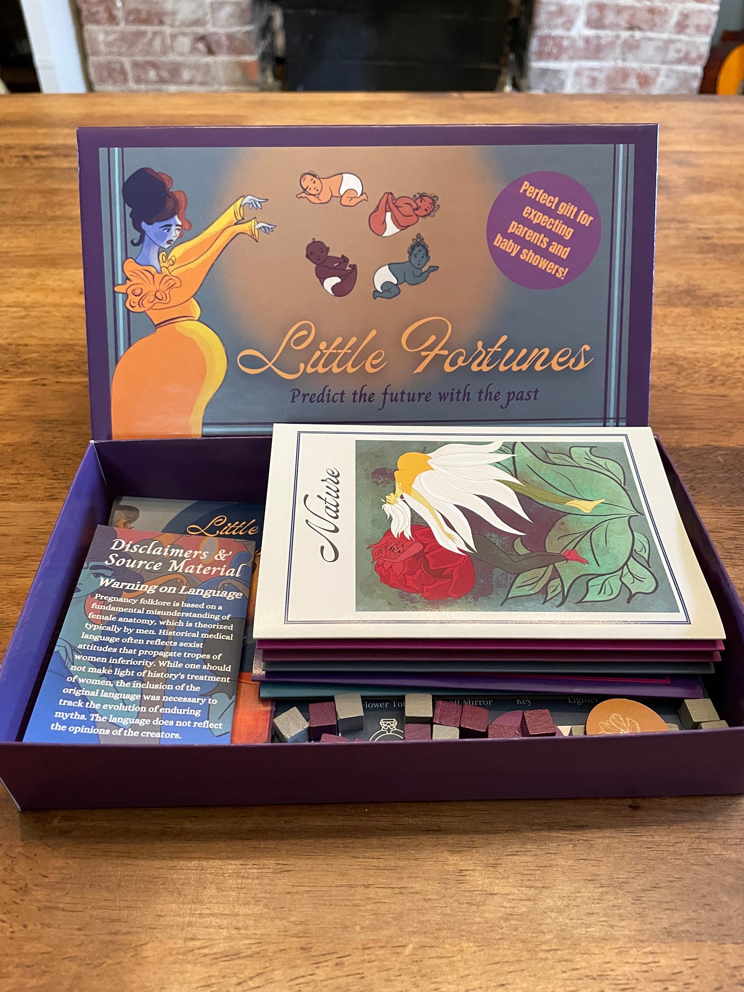 Game box showcasing pregnancy old wives tales and myths including a fortune teller with babies. The game box is opened and displays game components and beautiful art work.